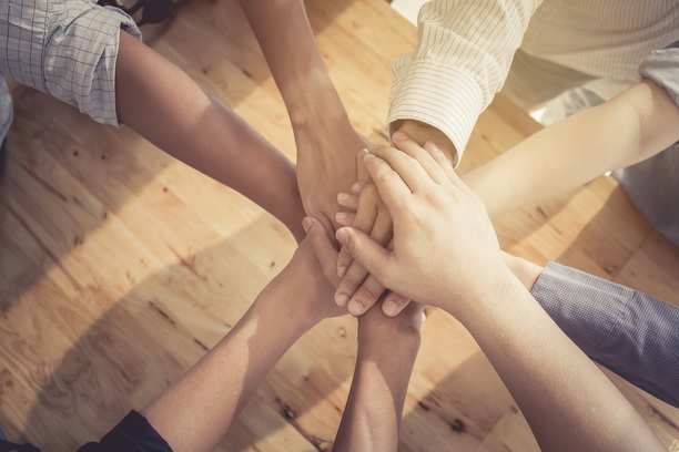 several people in a circle touch hands